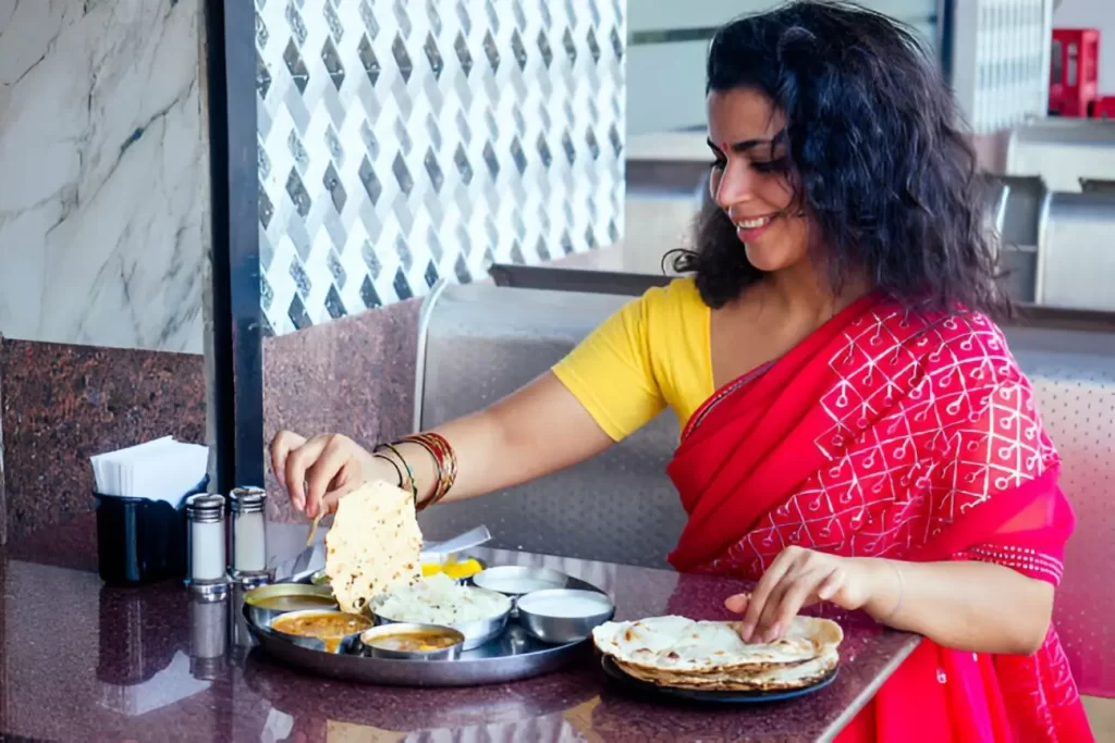 Beautiful brunette woman in red sari eating with appetite traditional thali wirh rise,curd,dal