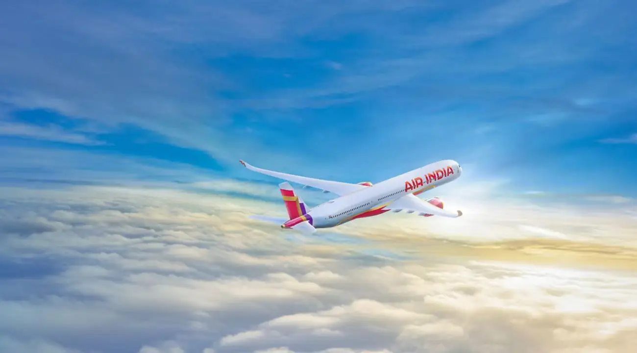 Air India airplane flying over clouds with a clear blue sky in the background.