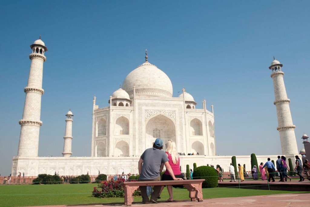 A tourist couple is enjoying the view of the Taj Mahal while sitting in the lush garden area