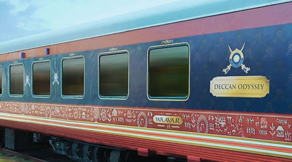  Luxurious Deccan Odyssey train with a blue and maroon exterior, displaying a golden nameplate and traditional decorative patterns, representing high-end train journeys in India.