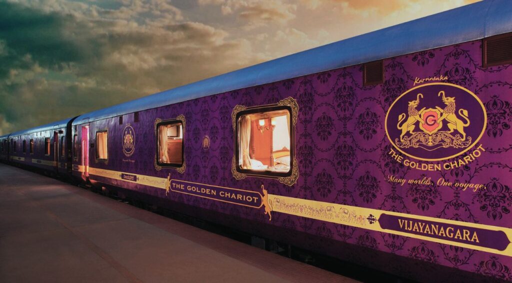  Luxurious Golden Chariot train with purple and gold exterior, displaying intricate patterns and a lion emblem, parked at a platform at sunset, symbolizing India's regal train journeys