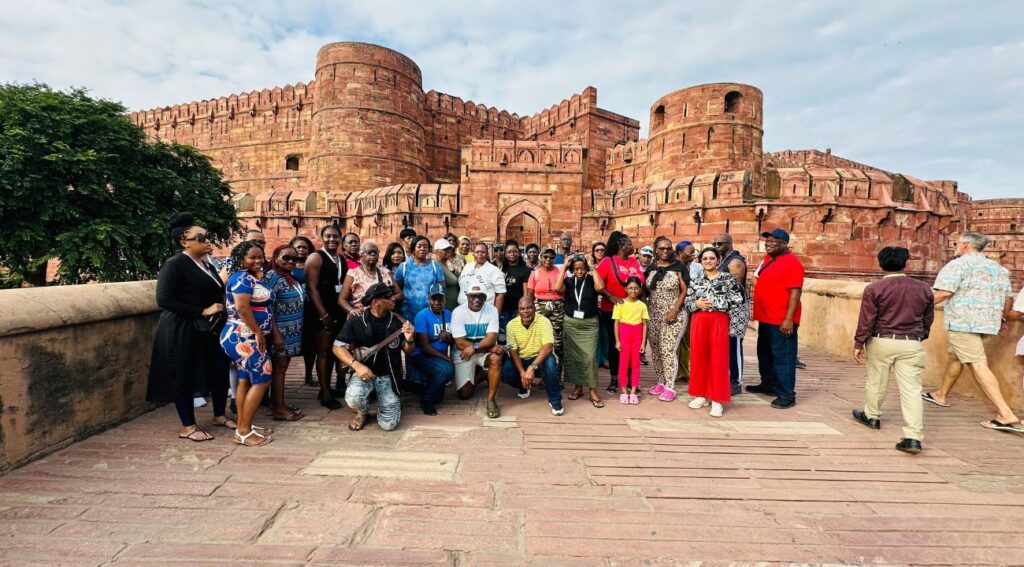 A group of tourists posing at Agra Fort during their India tour, with the red sandstone walls and towers of the fort visible in the background.