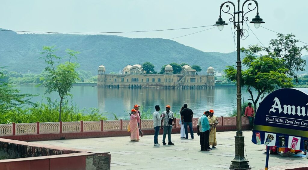 Tourists viewing Jal Mahal in the middle of a lake with hills in the background during a Golden Triangle tour in Jaipur.