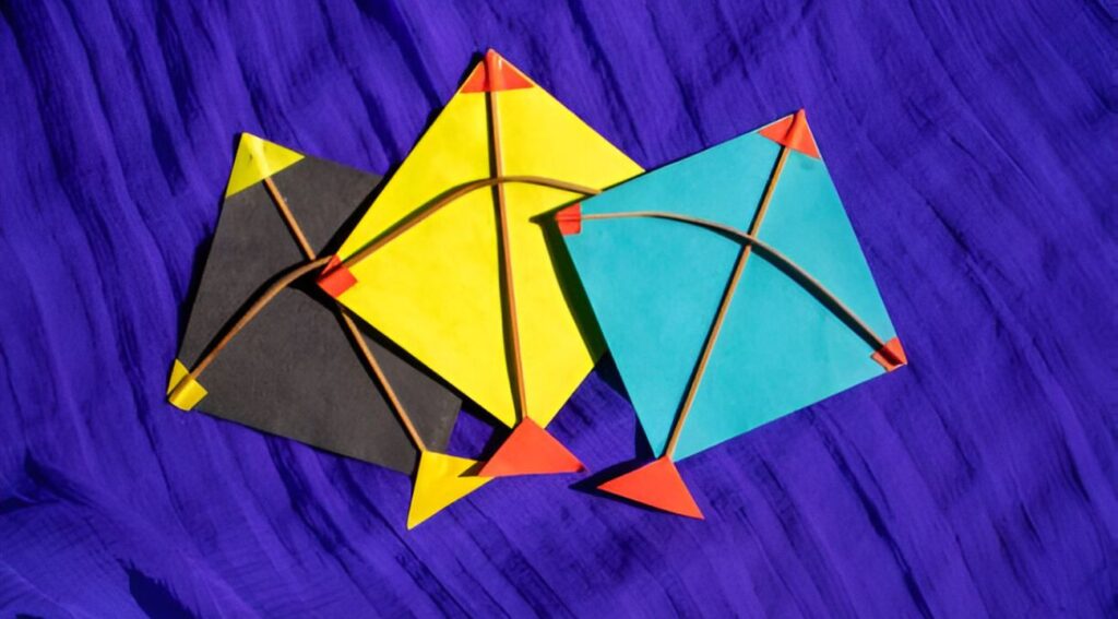 Three colorful kites in yellow, blue, and black arranged on a vibrant blue background.