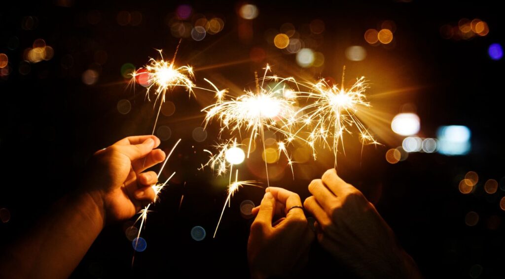  Hands holding sparklers glowing against a dark, festive background.